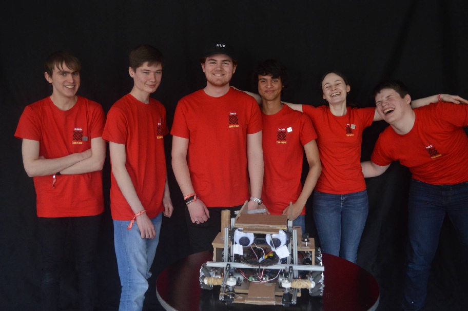 A team of students looking happy standing behind their robot