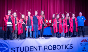 The competitors from Gymnasium Markt Indersdorf wearing red capes with black dots, standing with their ladybird themed robot and guest speaker from the Raspberry Pi Foundation.